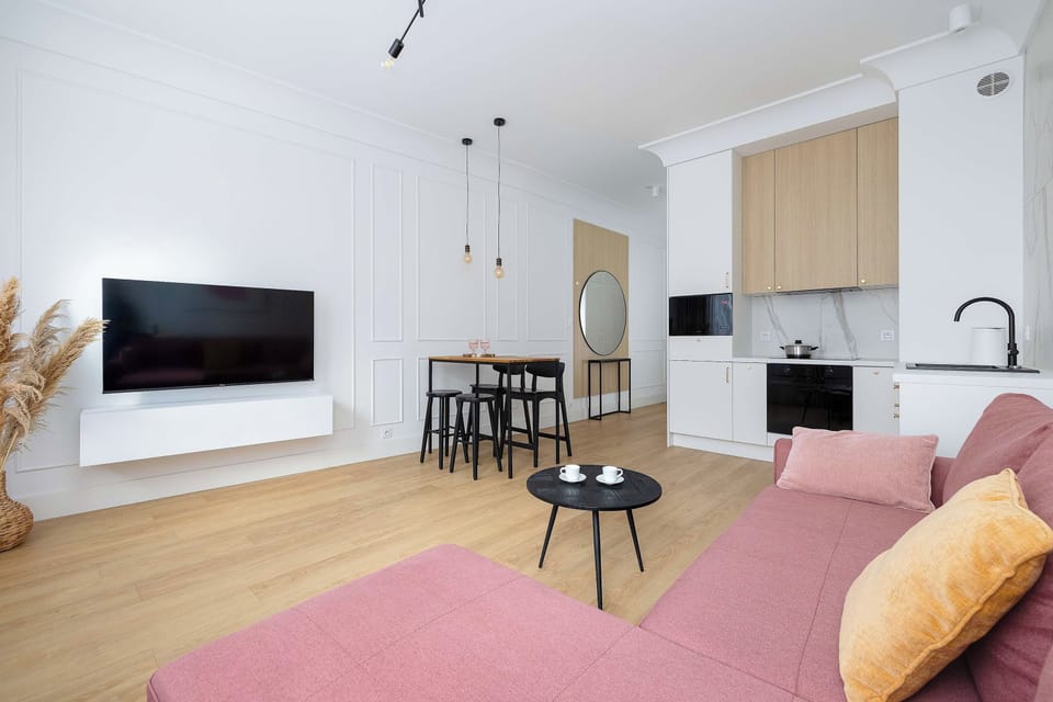 A cozy living area with a wall mounted TV, pink sofa and small coffee table. The open layout provides a pleasant space for relaxing and watching your favorite shows.