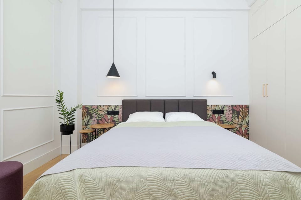 A bright bedroom with a double bed, soft bedding and minimalist wall decor. The neutral colors and gentle lighting create a relaxing atmosphere.