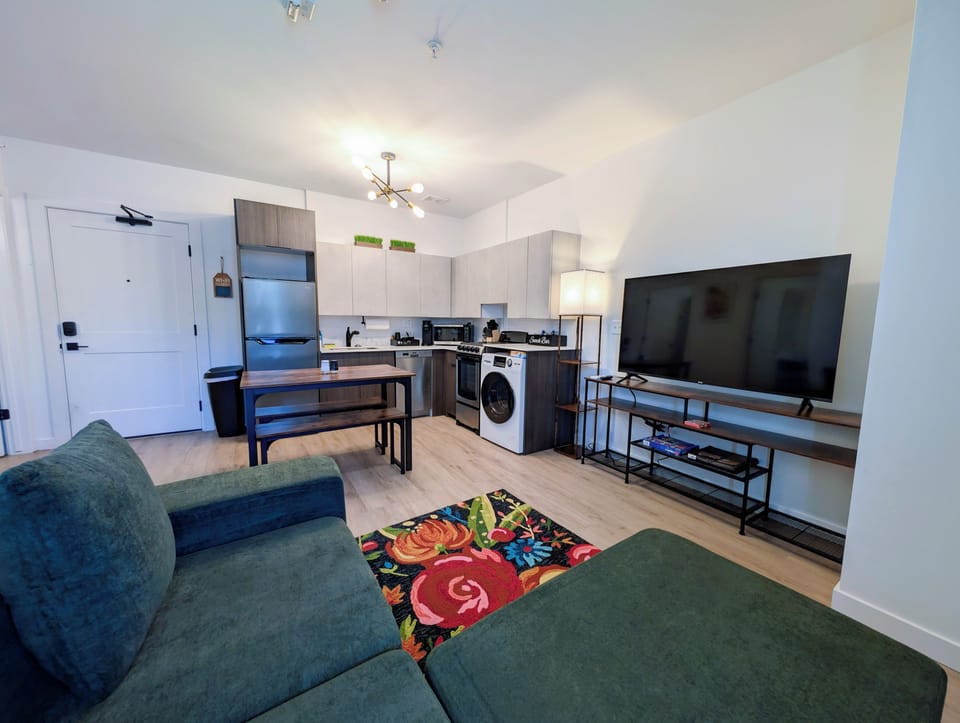 Modern open-concept living space with large TV and in-unit washer