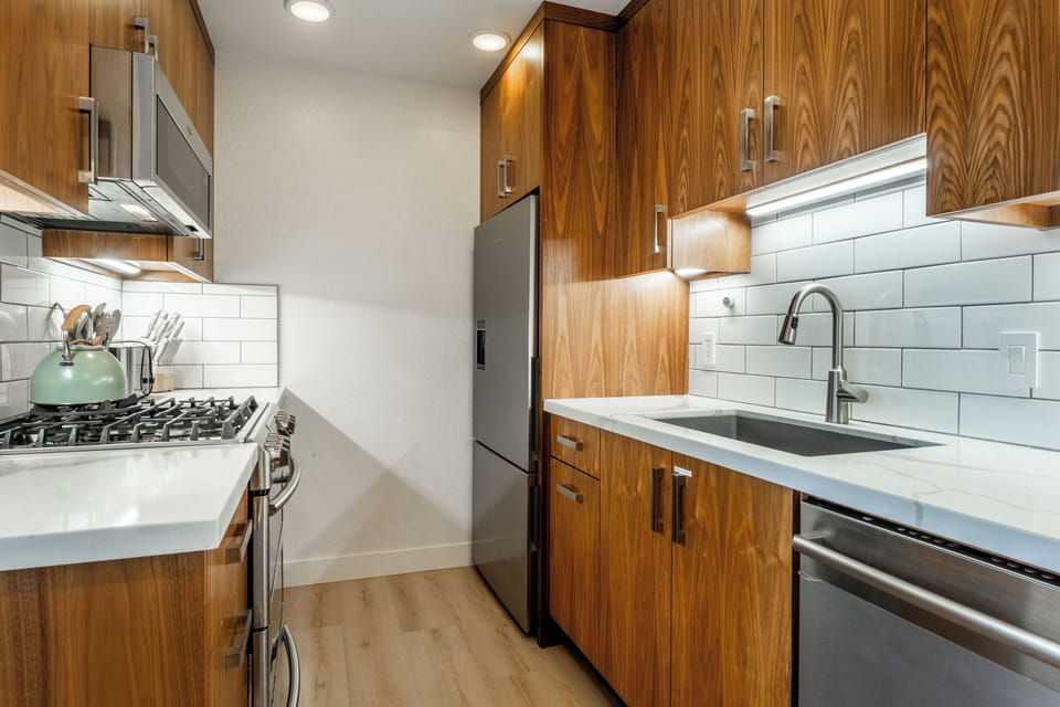 A sleek galley kitchen awaits, with warm wood cabinetry, stainless appliances, and clean subway tile backsplash—everything you need to whip up your vacation meals.