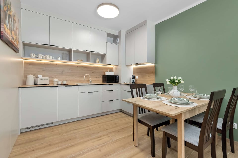 A modern open-plan kitchen and dining area with white cabinetry and light wooden flooring. A dining table with chairs is positioned next to the kitchen, creating a practical shared space.