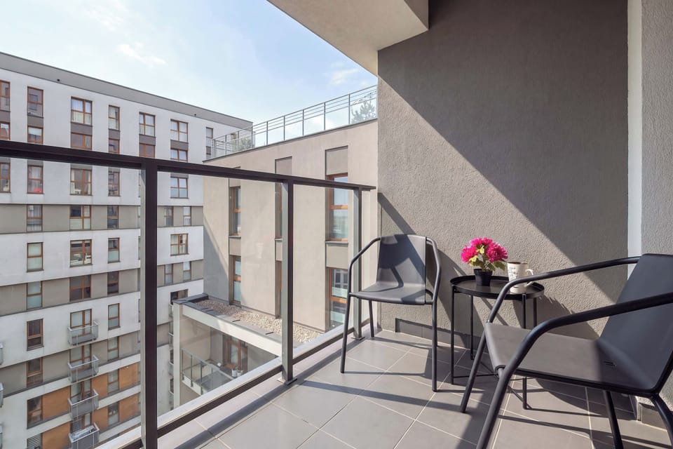 A private balcony with a small outdoor table and two chairs. The balcony overlooks the surrounding residential buildings and offers an open view of the neighborhood.