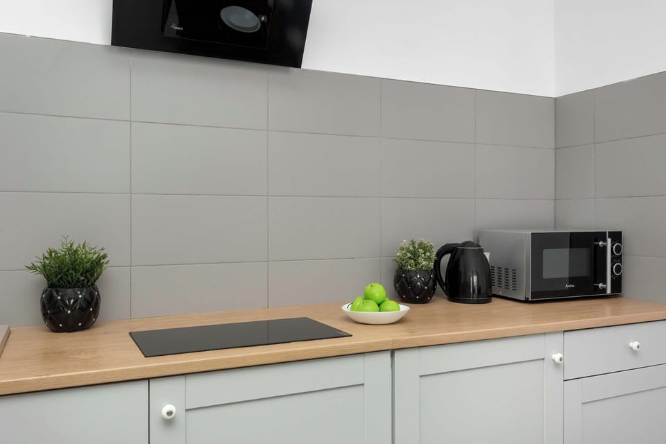 A modern kitchen with white cabinets, a light countertop, and a black induction cooktop. A microwave and small decorative plants are placed on the counter, creating a clean and functional space.