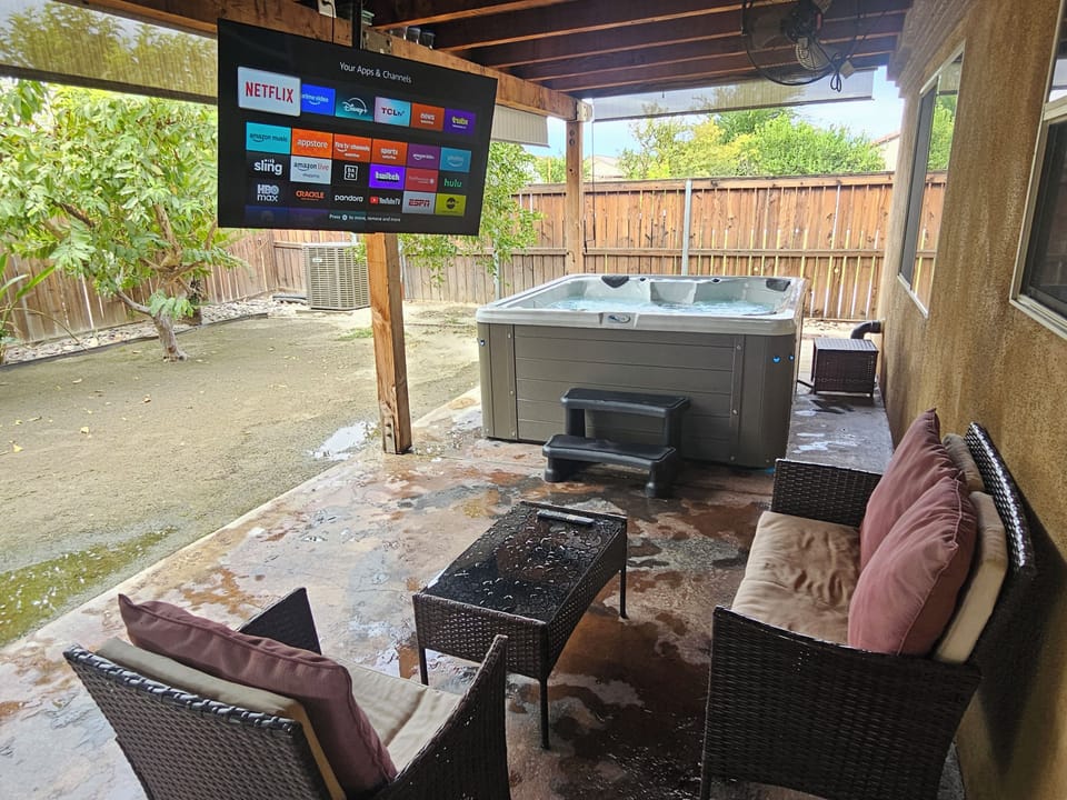 Private backyard retreat with hot tub, TV, and covered seating.