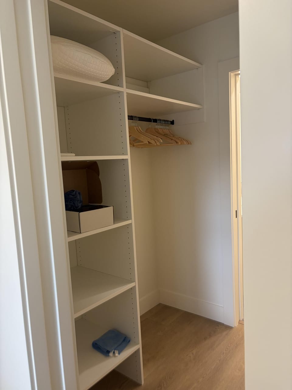 White built-in shelving and a black hanging rod with wooden hangers in a walk-in closet with wood flooring.