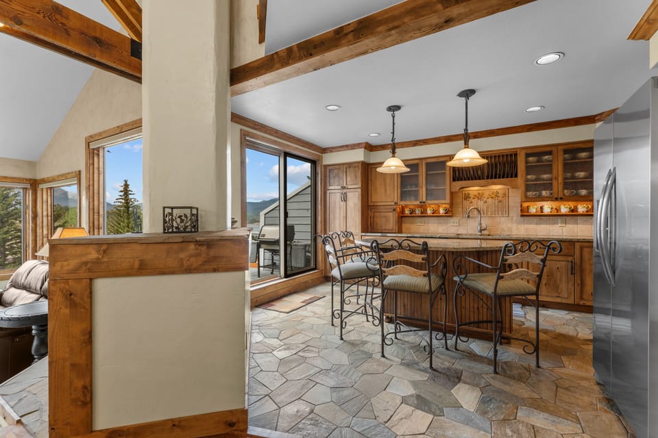 Gather around the rustic wood island in your fully-equipped kitchen, where exposed beams frame stunning mountain views through expansive windows. Step outside to your private balcony and breathe in the alpine air.