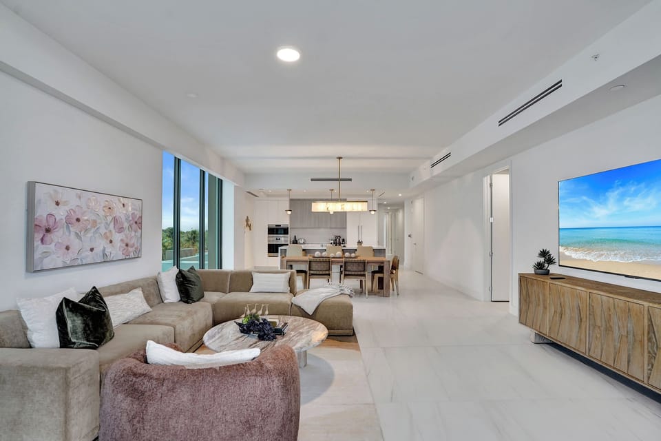 Open-plan living and dining with ocean-view TV art, sectional sofa, and kitchen beyond.