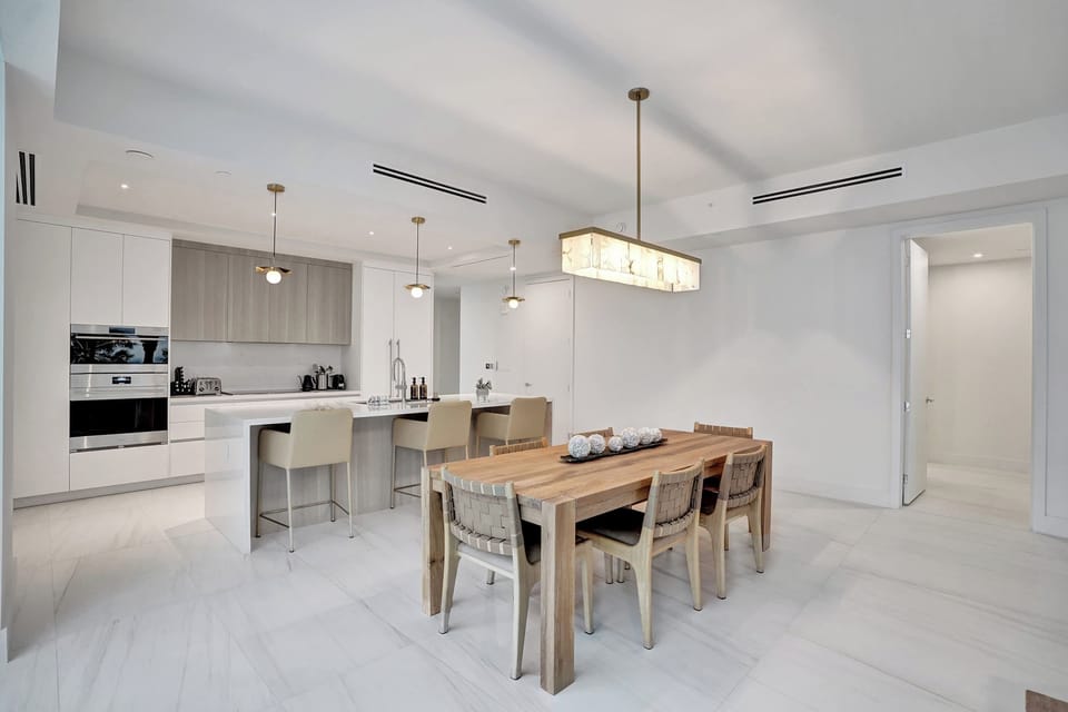 Dining area with wooden six-seat table under a rectangular chandelier, open to the kitchen.