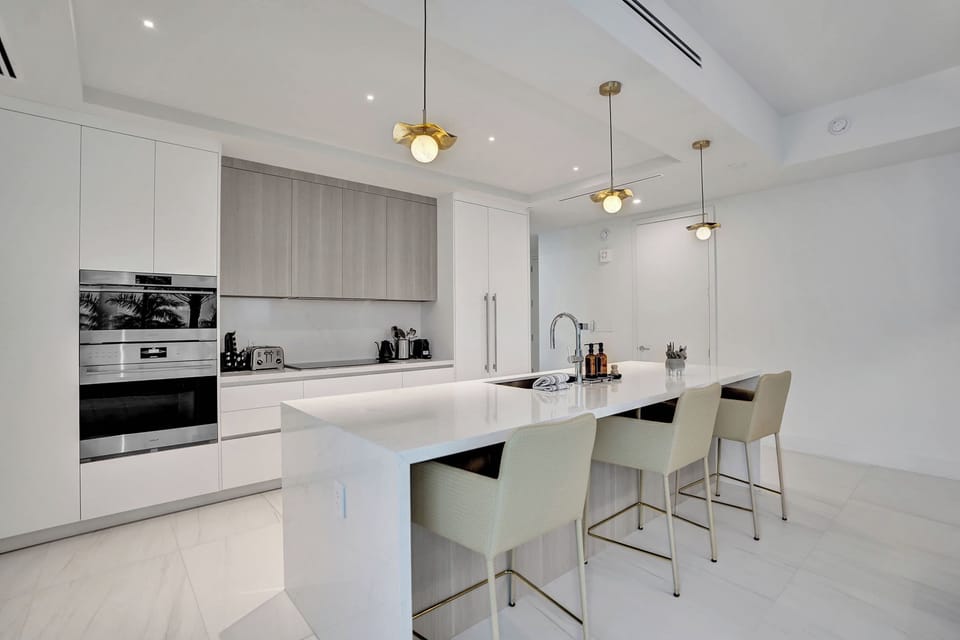 Chef's kitchen with waterfall quartz island, bar seating, built-in ovens, and white cabinetry.