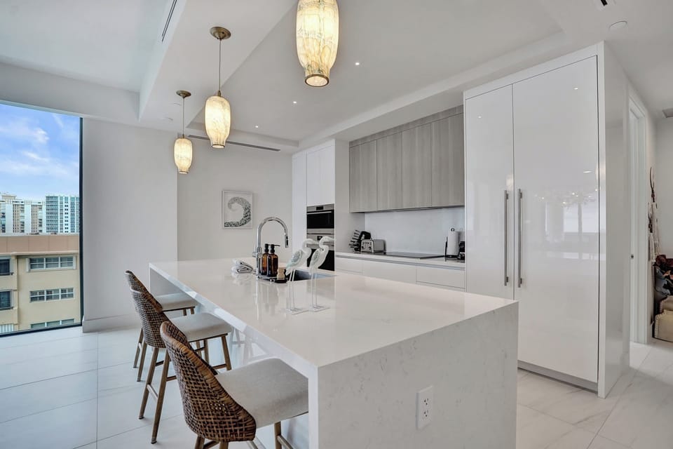 Kitchen island with rattan bar stools beside a window with city views, pendant lights above.
