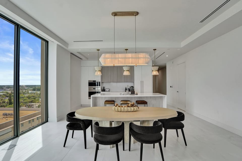 Open dining area with oval table, six chairs, and floor-to-ceiling windows overlooking the city skyline.