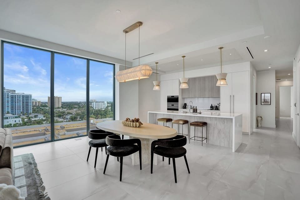 Open dining and kitchen with floor-to-ceiling windows overlooking the city and coastline.