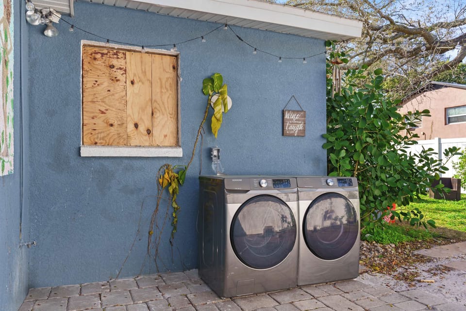 Modern washer and dryer sit ready in your private outdoor laundry area, accented by soft string lights and cheerful greenery. Conveniently placed just steps from your door, making laundry day effortless.