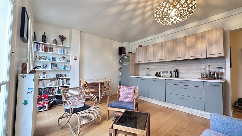 Séjour lumineux avec cuisine équipée ouverte, parquet et coin salon cosy — appartement Paris 19 près du Canal / Bright open-plan living room with fully equipped kitchen and cosy seating area — apartment in Paris 19 near the Canal