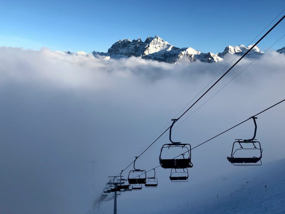 Alpine chairlift rising above the clouds with dramatic Haute-Savoie mountain peaks in the distance.