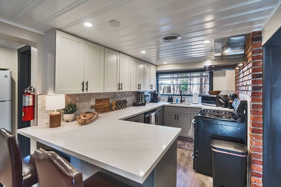 Warm wood cutting boards and cozy accents style the waterfall peninsula, framed by a striking exposed brick wall. A vintage stove and hexagon-tiled backsplash bring character to this thoughtfully renovated space.
