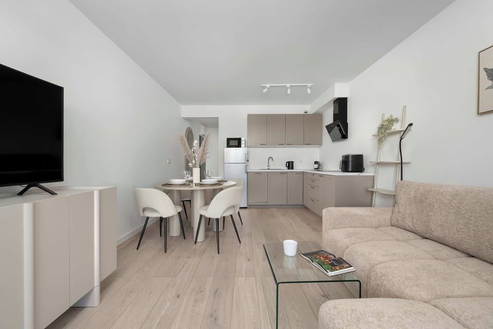 An open-plan living and dining space featuring a sofa, TV, dining table, and modern kitchen.