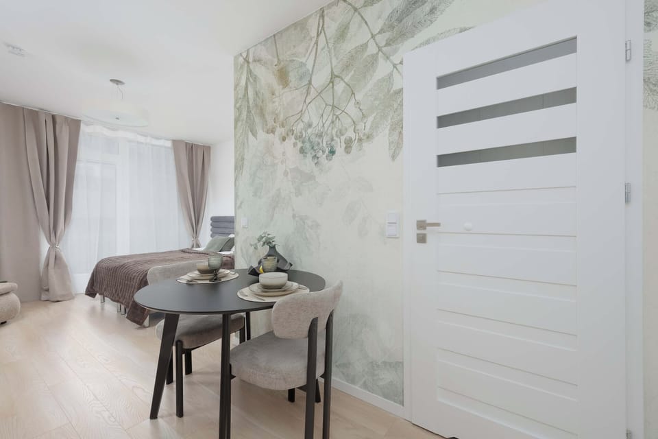 Decorative studio corner highlighted by nature-inspired botanical wallpaper next to a classic white interior door and a dining set.