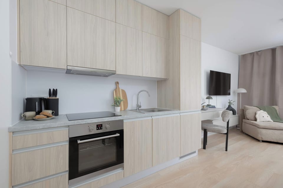 Modern and minimalist kitchenette featuring light wood cabinetry, sleek countertops, and integrated appliances. 