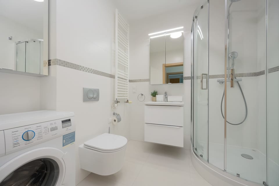 Clean, modern bathroom with shower, toilet, washbasin, mirrored cabinets, and washing machine.