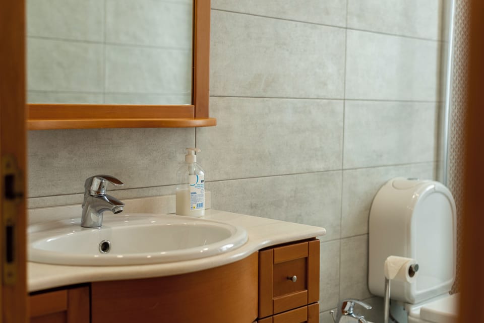 Clean tiled bath with wood vanity, mirror, and stocked essentials.