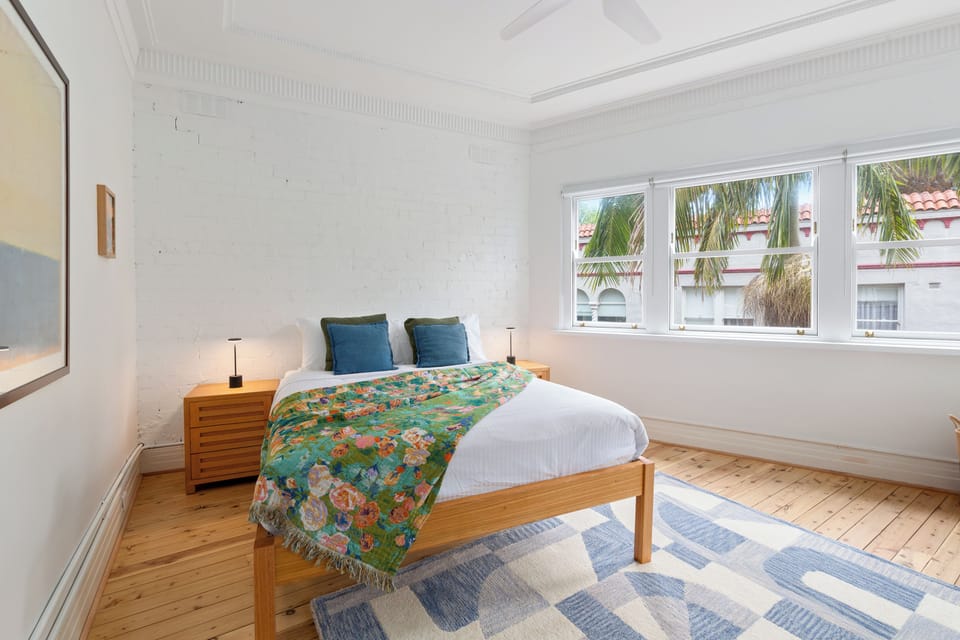 Recharge in the bedroom, where a queen bed, colourful textiles and abundant natural light create a bright retreat, with air conditioning and a ceiling fan adding extra comfort.