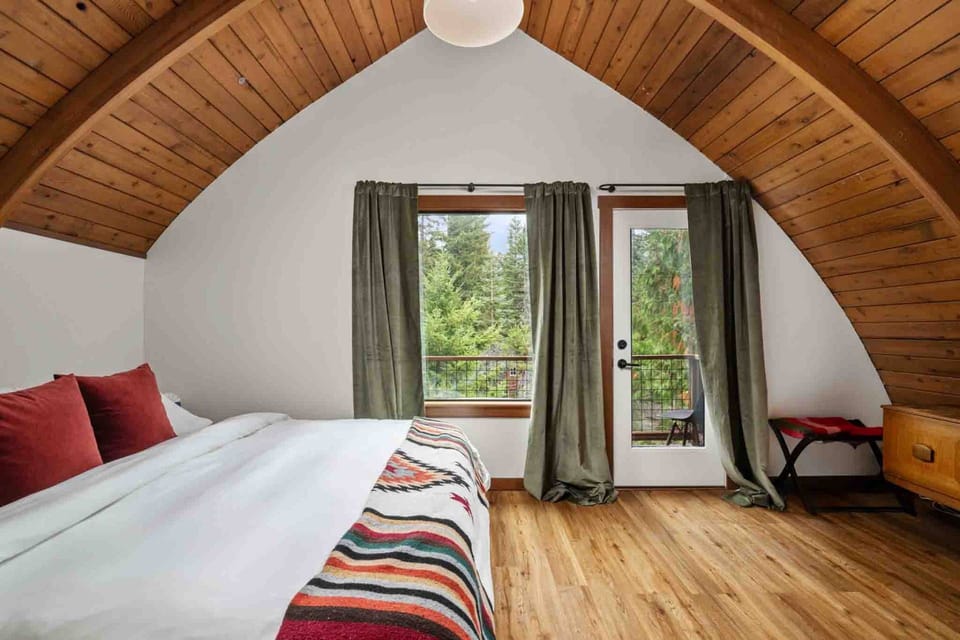 Cozy loft bedroom with vaulted wood ceilings, a king bed with patterned throw blankets, and private balcony access.