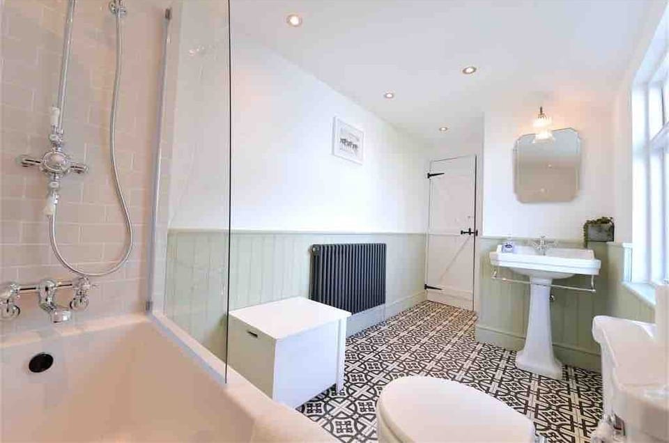 A light, spacious bathroom with a classic English feel, finished in soft green tones. Georgian-inspired details sit alongside a modern bath with shower over, creating a space that is bright, practical, and comfortable for everyday use.