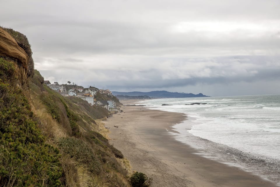 Coastal property nestled along a serene sandy beach, where gentle waves meet the shore beneath dramatic skies and scenic cliffs stretch into the distance.