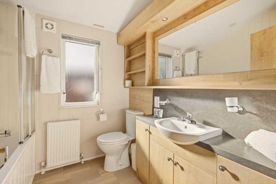 Bathroom with wash basin, large mirror, wooden cabinets and window