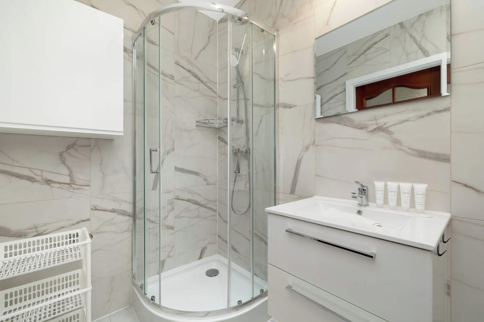 A modern bathroom with marble-patterned wall tiles, a glass-enclosed shower, and a white vanity with a sink. 