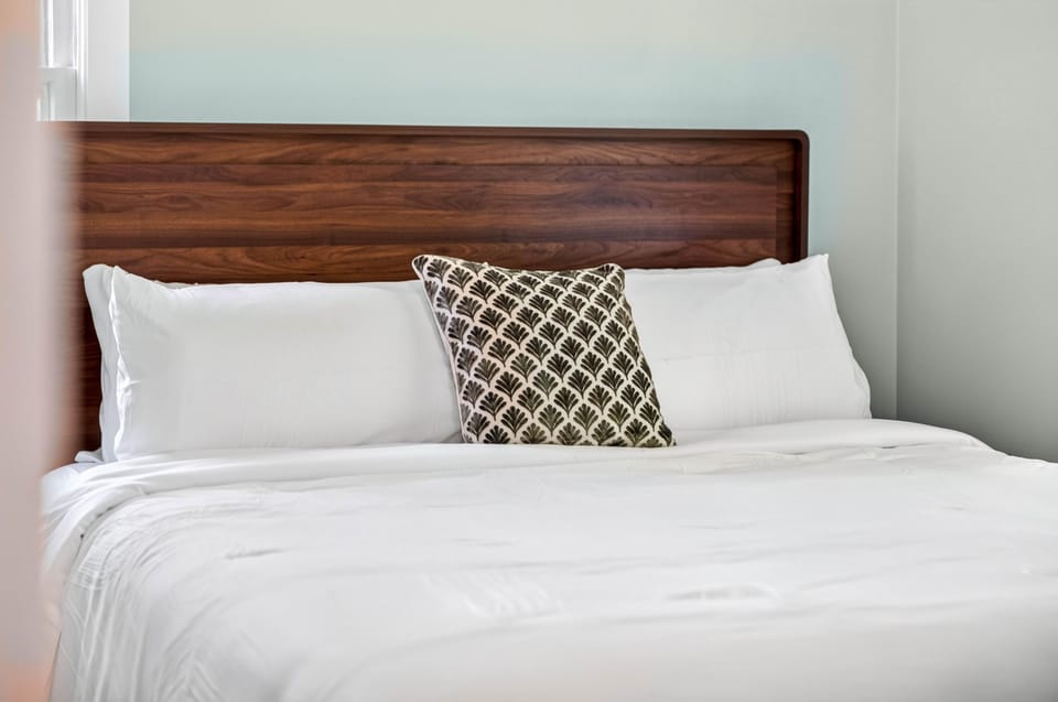 King bed with smooth walnut headboard, crisp white linens, and a black-and-white patterned accent pillow.