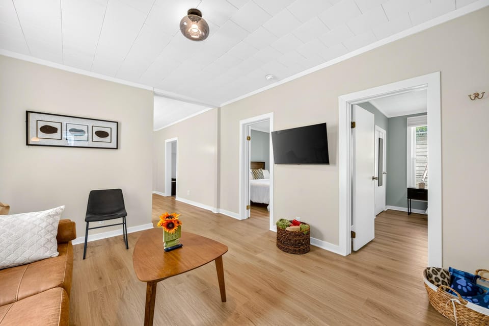 Living room with light wood floors, a leather sofa, triangular wood coffee table, and wall-mounted flat-screen TV.