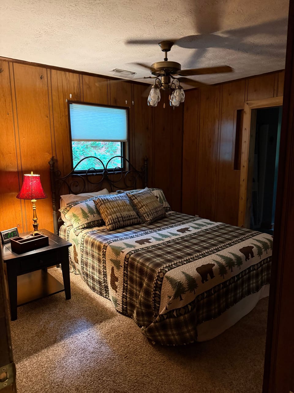 A wood-paneled bedroom features a bed with woodland bedding and a ceiling fan.