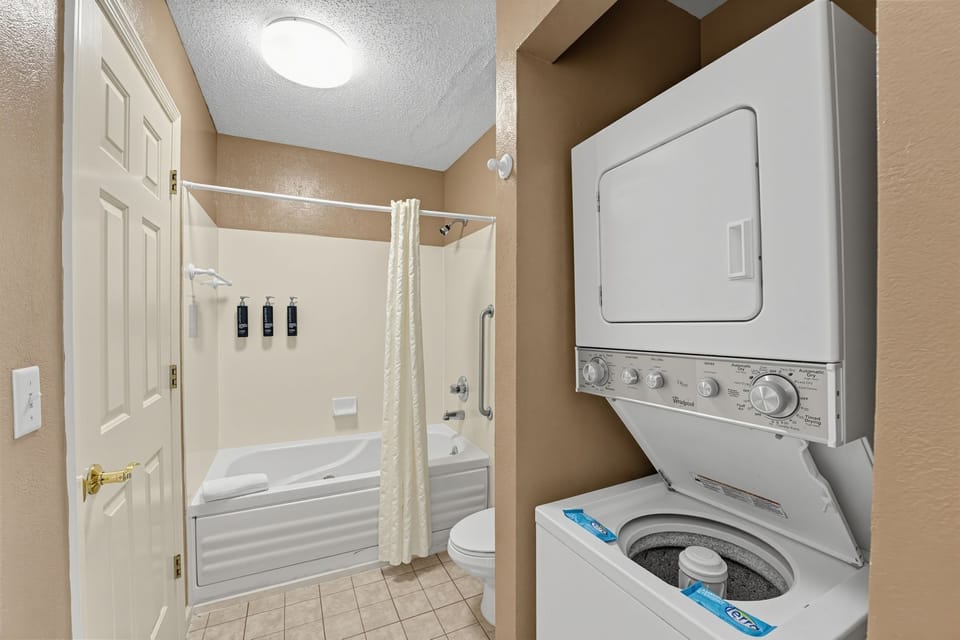 Bathroom with a tub, shower curtain, and a stacked washer and dryer.