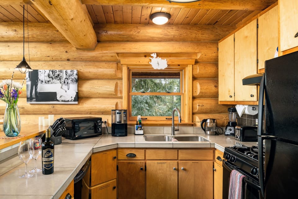 Kitchen with double sink, forest-view window, small appliances, and gas range