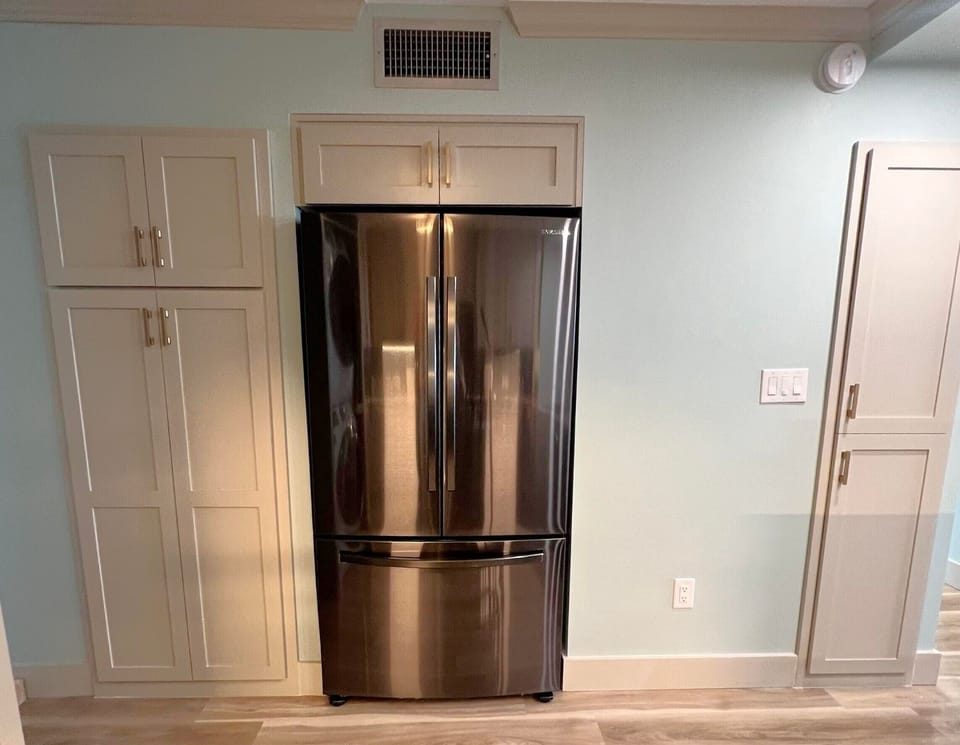 Fridge freezer flanked by broom closet and storage pantry 
