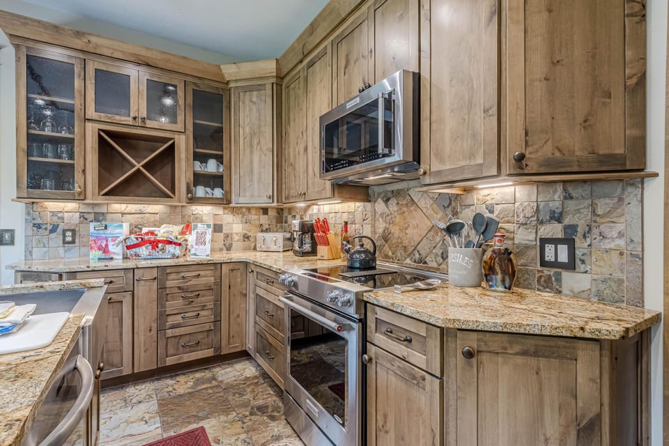 Rustic kitchen corner with granite counters, slate tile backsplash, stainless steel stove, and wood cabinetry.