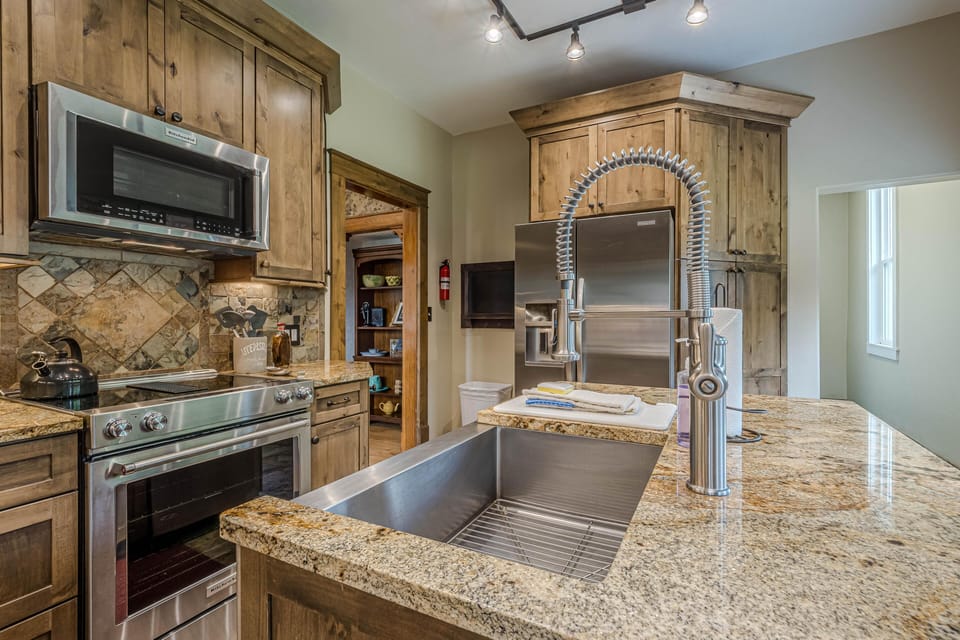 Stainless steel sink with spring coil faucet sits in granite countertop surrounded by rustic wood cabinetry.