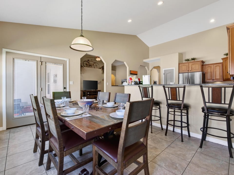 Rustic wooden dining table set for six sits adjacent to a breakfast bar with four dark wood stools.
