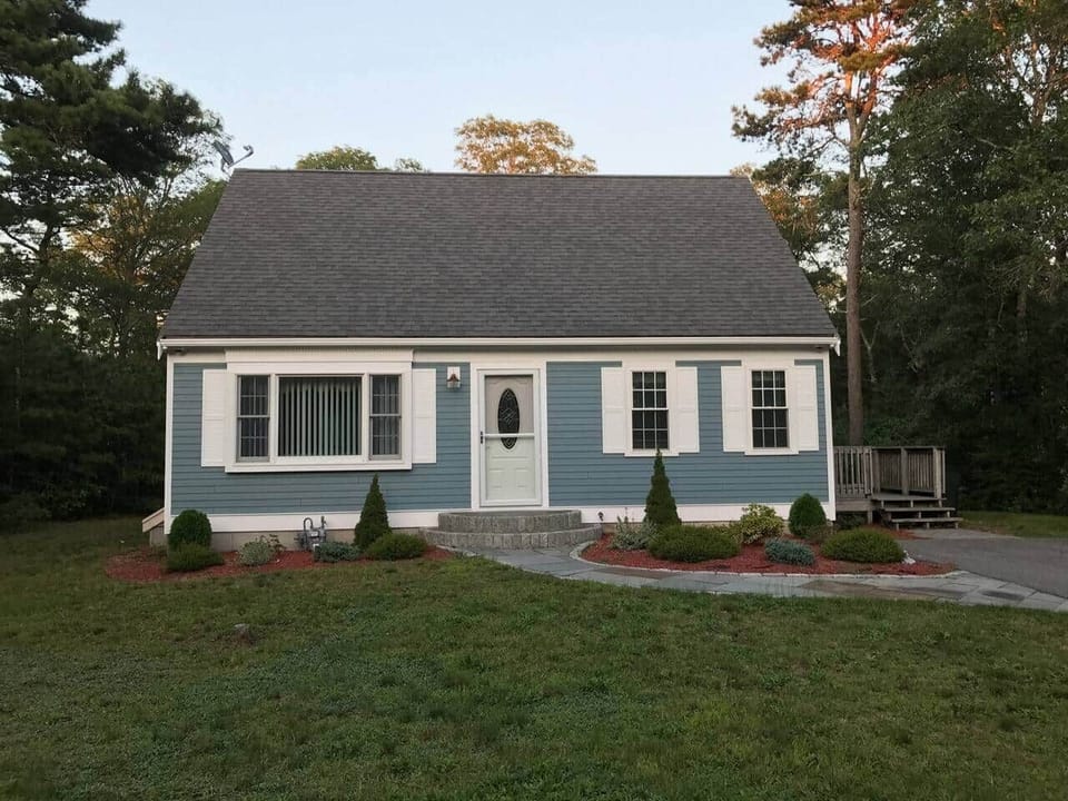 Charming exterior with lush greenery and welcoming lighting, your Cape Cod vacation haven from the moment you arrive.
