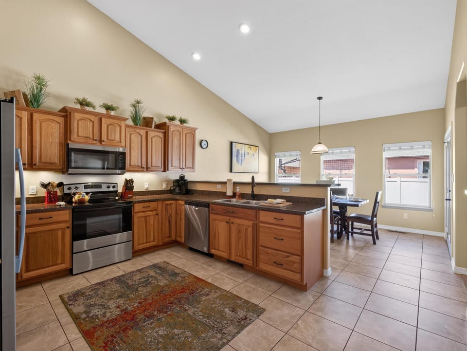 Maple cabinetry and granite countertops wrap the kitchen, with stainless steel appliances and a tile floor rug anchoring the space.