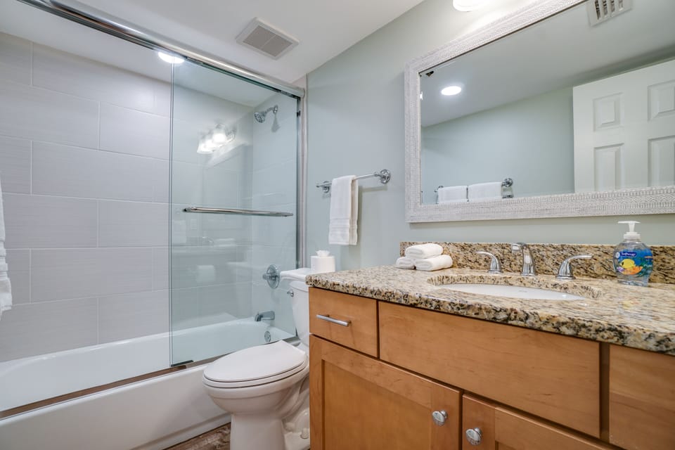 Second bathroom with tile shower surround and glass shower door.