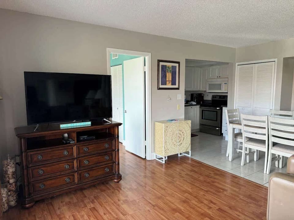 Open concept living room with flat-screen TV, steps from full kitchen.
