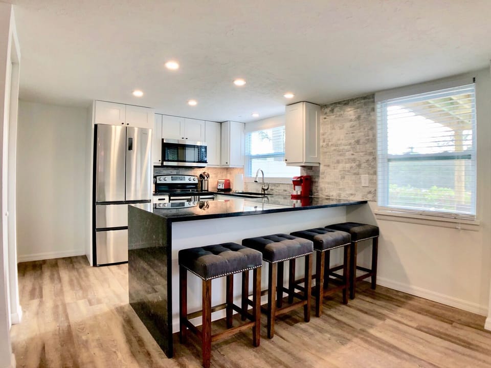 Kitchen with white cabinetry, island with bar stools, and stainless steel appliances