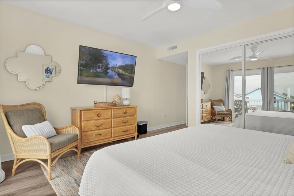 Unwind in your spacious bedroom featuring a wall-mounted TV and cozy reading chair for peaceful evenings.