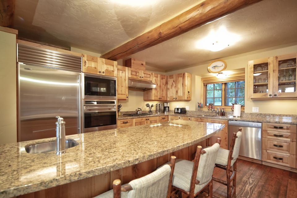 Your dream chef's kitchen awaits with gleaming granite countertops, professional-grade stainless steel appliances, and warm wood cabinetry under rustic exposed beams—perfect for creating memorable meals together.