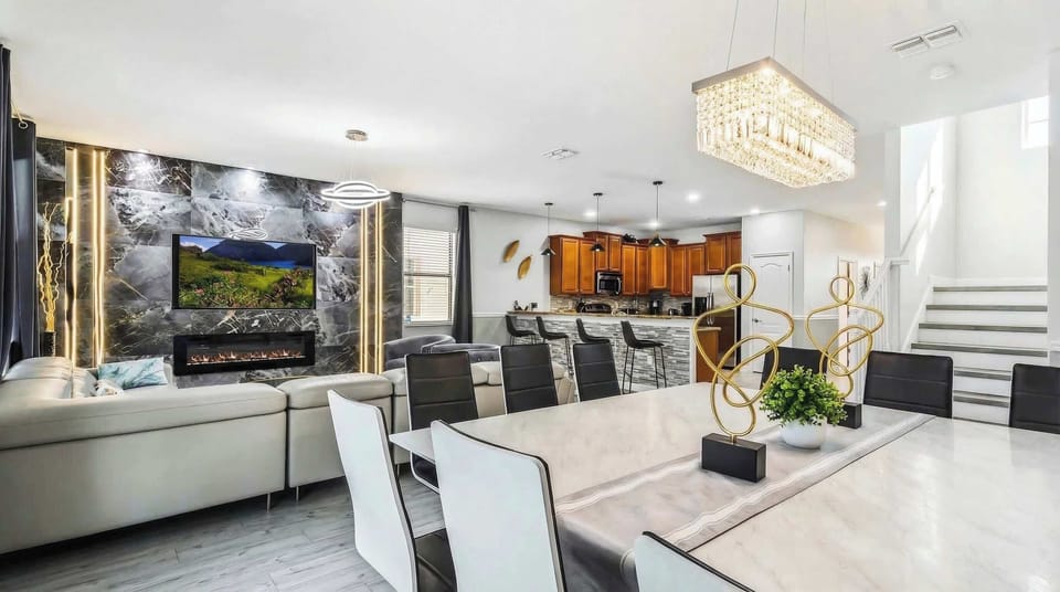 Elegant open-concept living area with a modern fireplace, marble accents, crystal chandelier, and a stylish kitchen.