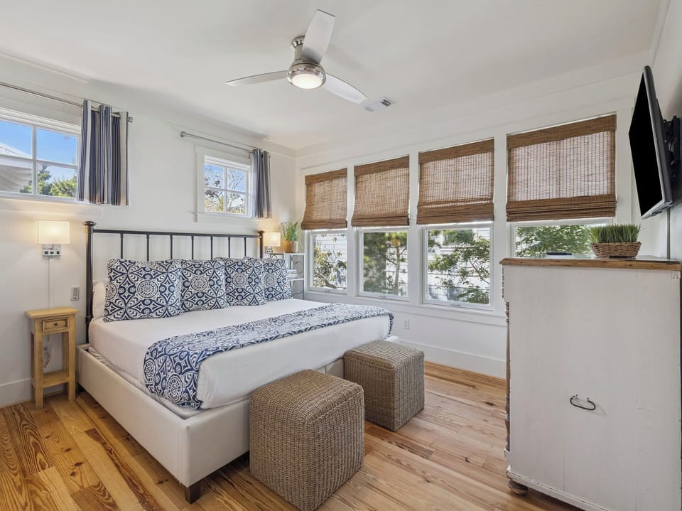 Rest peacefully in your bright bedroom featuring natural bamboo shades, cozy wicker seating, and a ceiling fan for comfort.