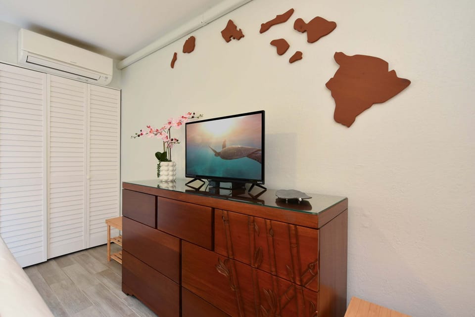 Enjoy your favorite shows on the bedroom flat-screen TV, set on a dark wood dresser beneath a wooden Hawaiian Islands wall display.